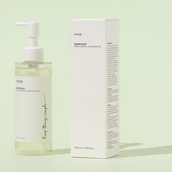 Anua Heartleaf Pore Control Cleansing Oil – ansigtsrens - gennemsigtig plastflaske med hvid pumpe og hvid etiket står oprejst på en lys baggrund. Ved siden af flasken står produktets papkasse, som er hvid med grønne og sorte detaljer.