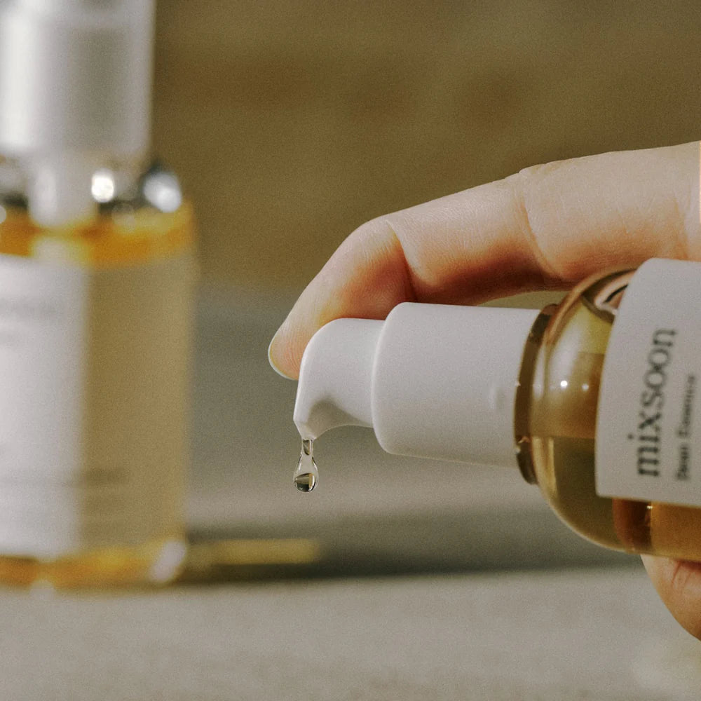en person pumper noget Mixsoon - 
Bean Essence - hudpleje essens ud .. man kan se persones finger og en flaske mixsoon i baggrunden