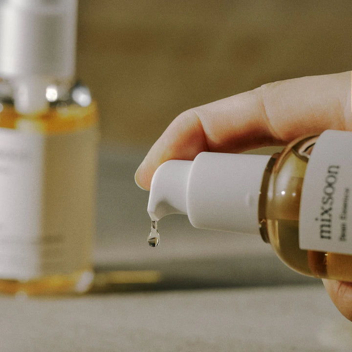 en person pumper noget Mixsoon - 
Bean Essence - hudpleje essens ud .. man kan se persones finger og en flaske mixsoon i baggrunden